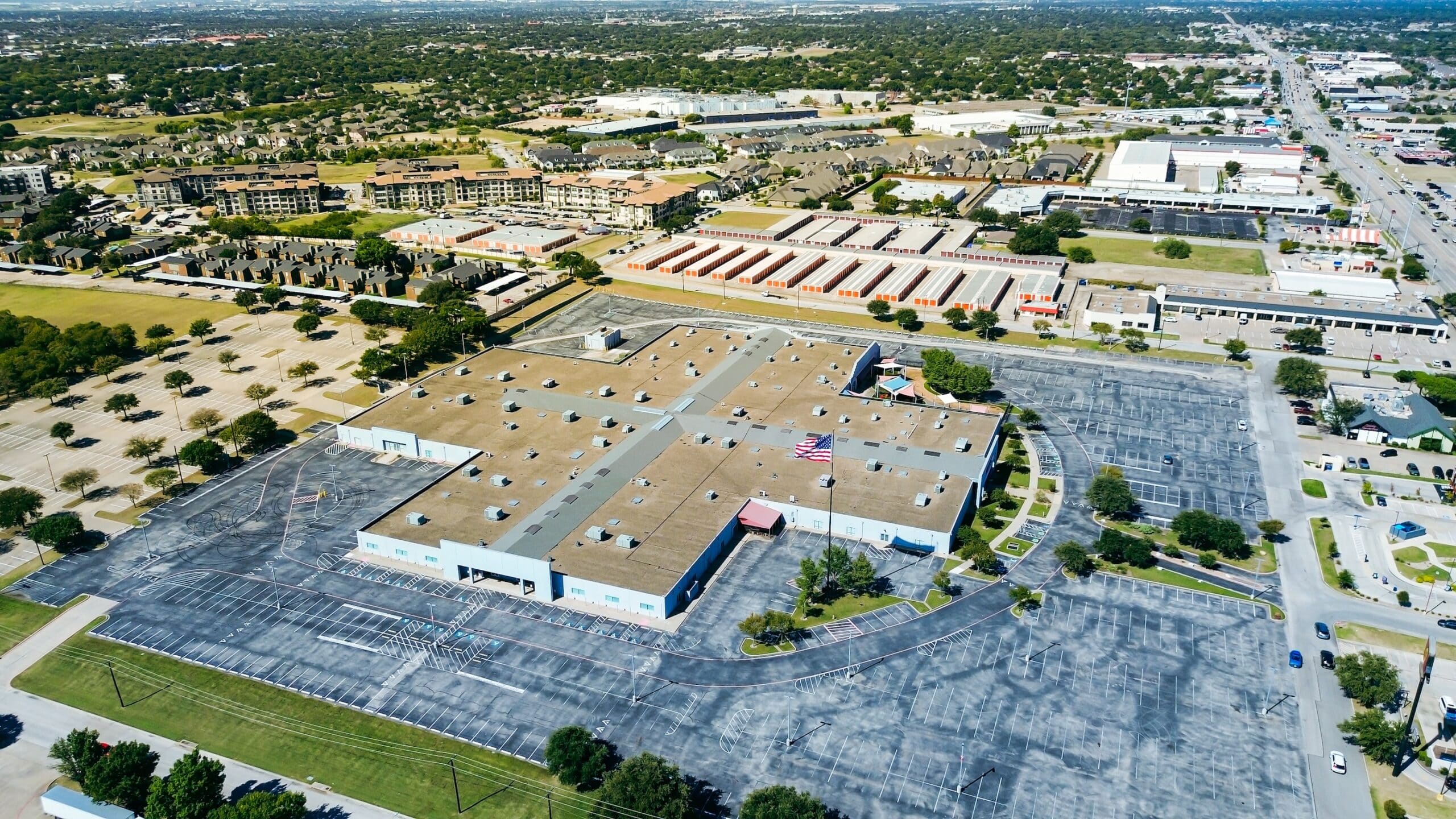 Industrial building flat roof HVAC units, unoccupied parking lot, adjacent storage facility, apartment complex, suburban homes near NE Loop 820 highway front retail pads, North Richland Hills, TX
